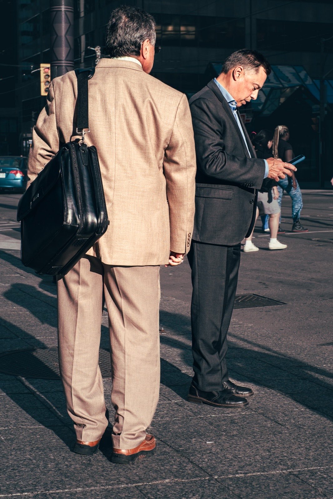 Two businessmen waiting at a downtown Toronto crosswalk in harsh evening sunlight.