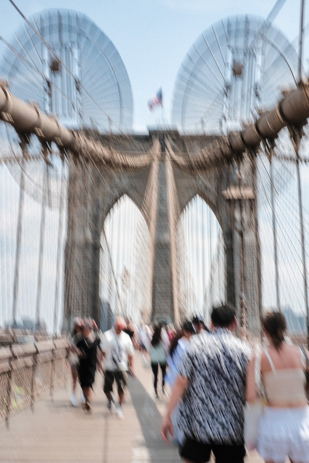 Pedestrians crossing the Brooklyn Bridge in motion blur beneath its stone arches.