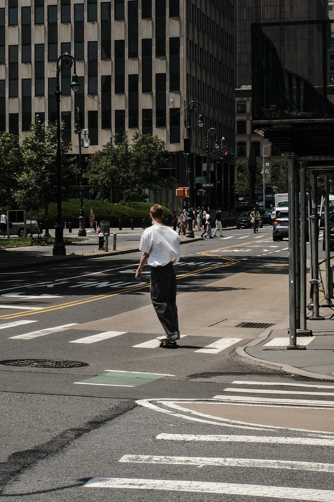 A skater crossing an empty crosswalk in harsh midday sun at Federal Plaza, New York.