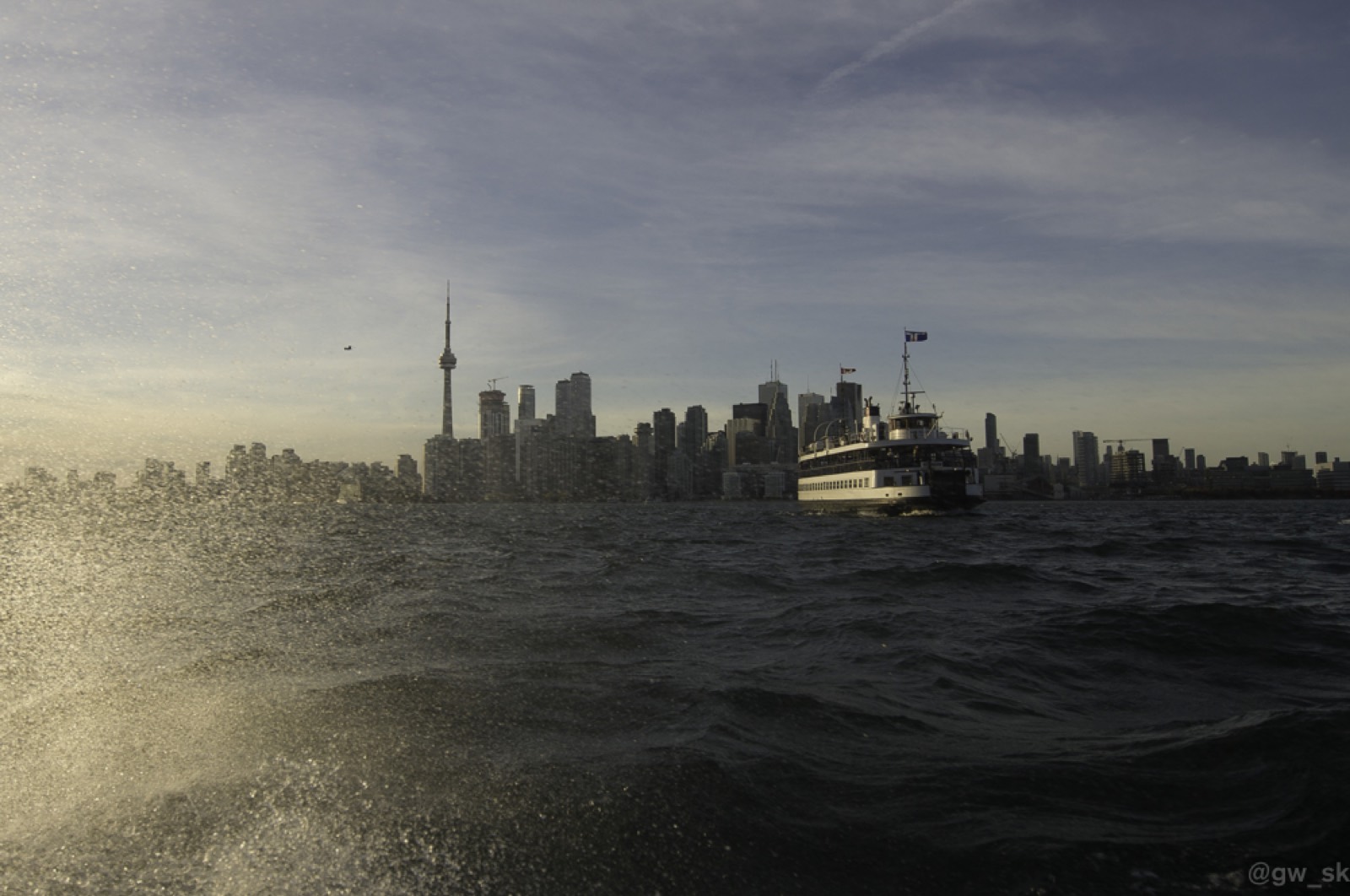 A Toronto Island ferry crossing the harbour at golden hour with the CN Tower and skyline behind.